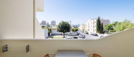 Un balcón con mesa y sillas, con vista a una calle con coches aparcados y edificios.