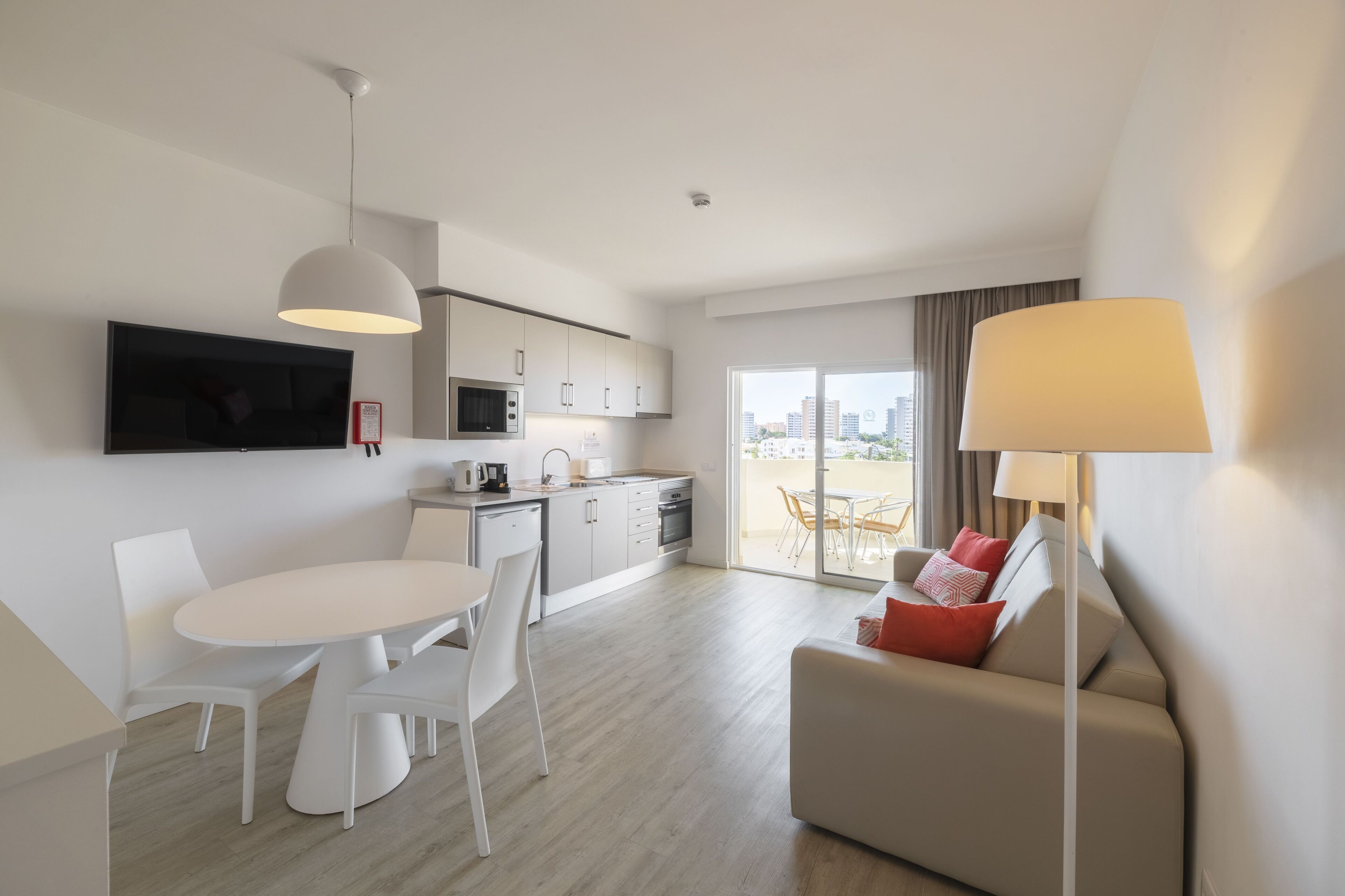 Una habitación de hotel moderna con zona de comedor, kitchenette y un sofá con lámpara.
