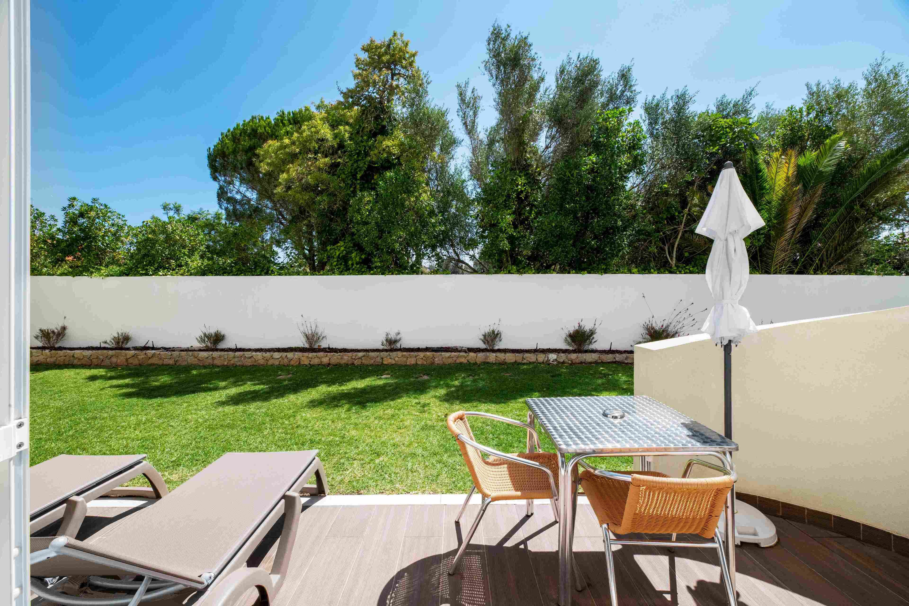 Une terrasse avec une table et des chaises, un mur blanc et une pelouse verdoyante.