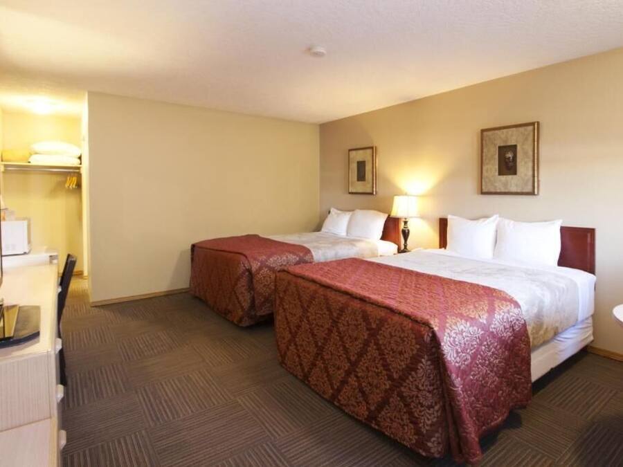 A hotel room with two beds, a desk, and a mirror.