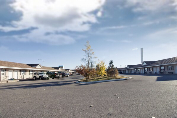 Un motel avec un parking, un petit arbre et, au fond, un grand immeuble.