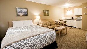 Ein Hotelzimmer mit Bett, Sofa, kleinem Tisch, Lampe und einer Küchenzeile mit Schränken und Mikrowelle.