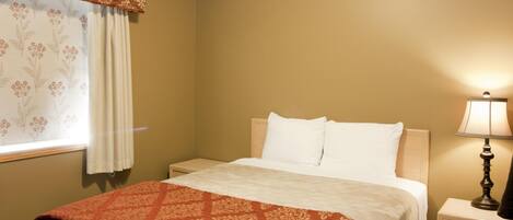A hotel room with a bed, a nightstand, a lamp, and a window with curtains.