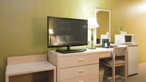 Ein Hotelzimmer mit Schreibtisch, Stuhl, Fernseher, Lampe, Mikrowelle und einem kleinen Schrank.