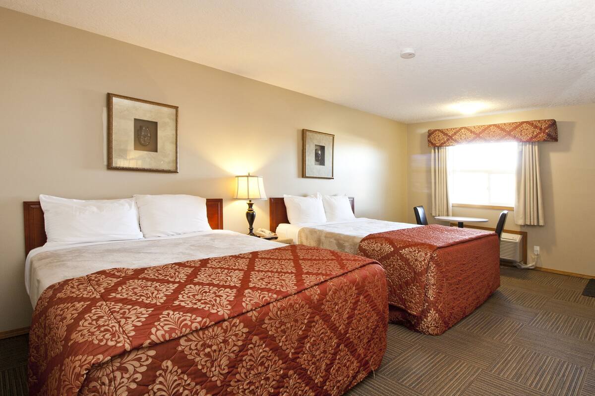 A hotel room with two beds, a small table, and a window with curtains.