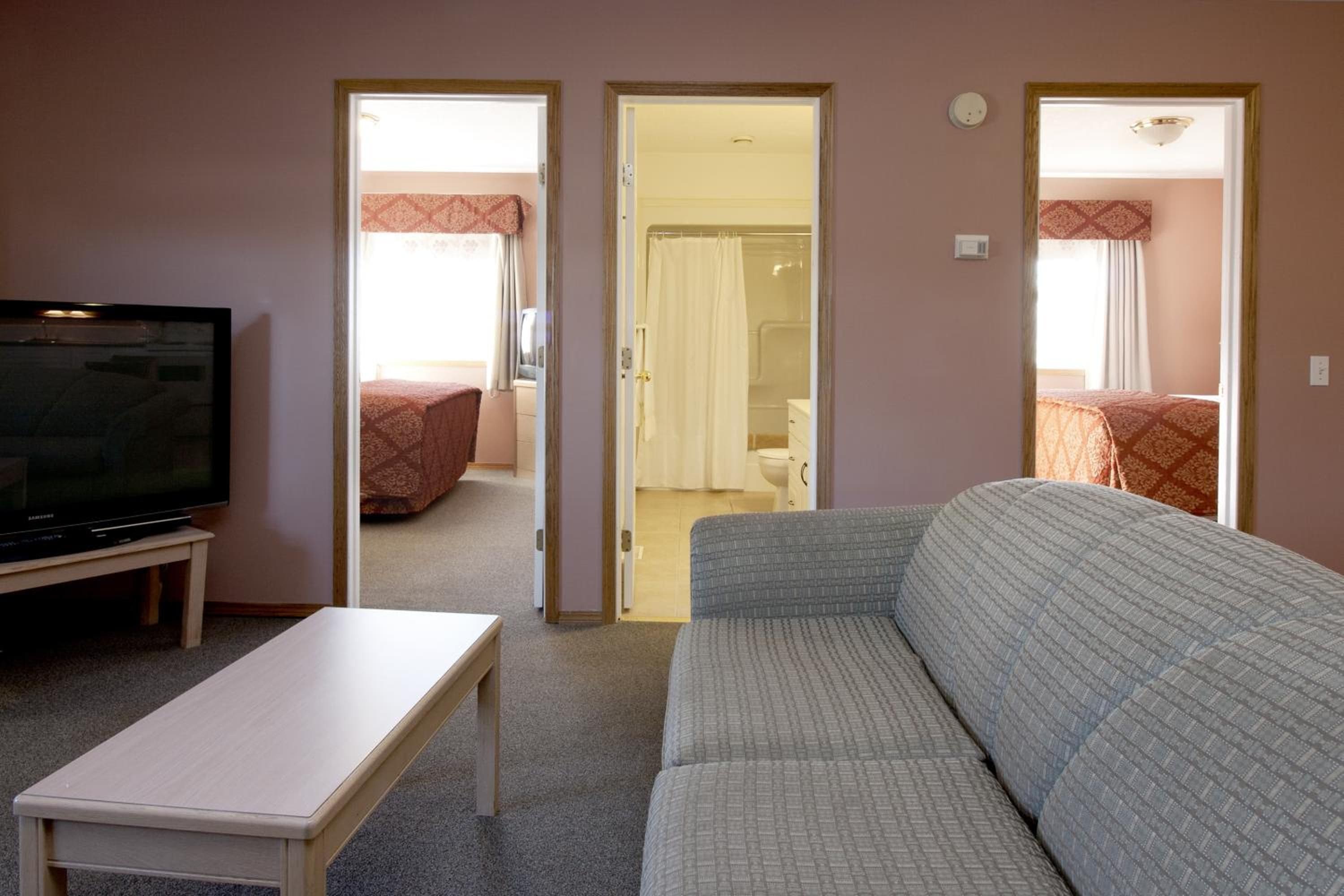 Een woonkamer met een televisie op een meubel, een bank en een bijzettafeltje. Er zijn twee deuren naar een slaapkamer en een badkamer.