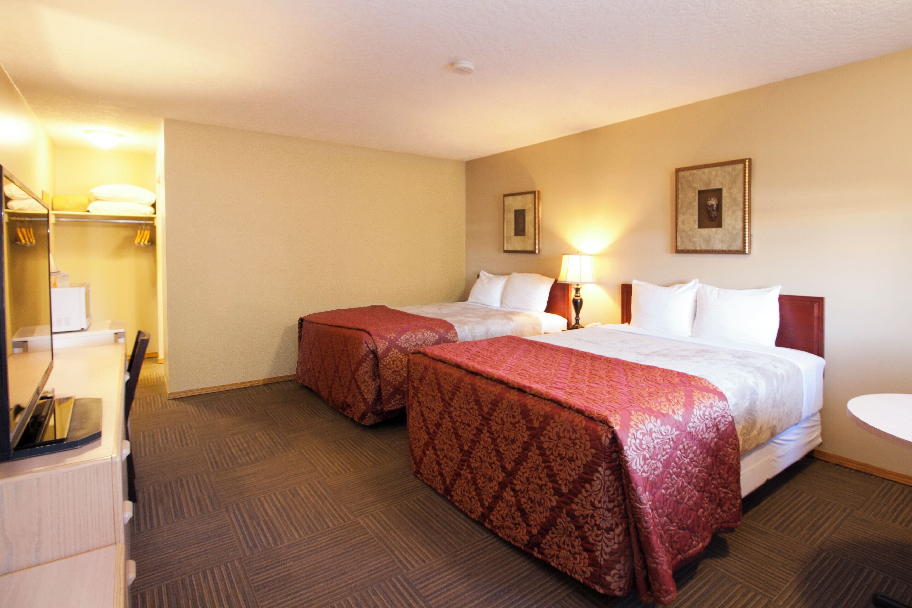 A hotel room with two beds, a desk, a chair, a lamp, and a small table.