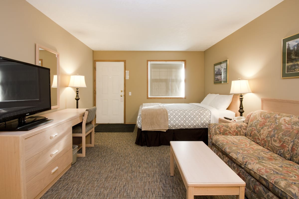 A hotel room with a bed, a sofa, a TV, a desk, and a lamp.