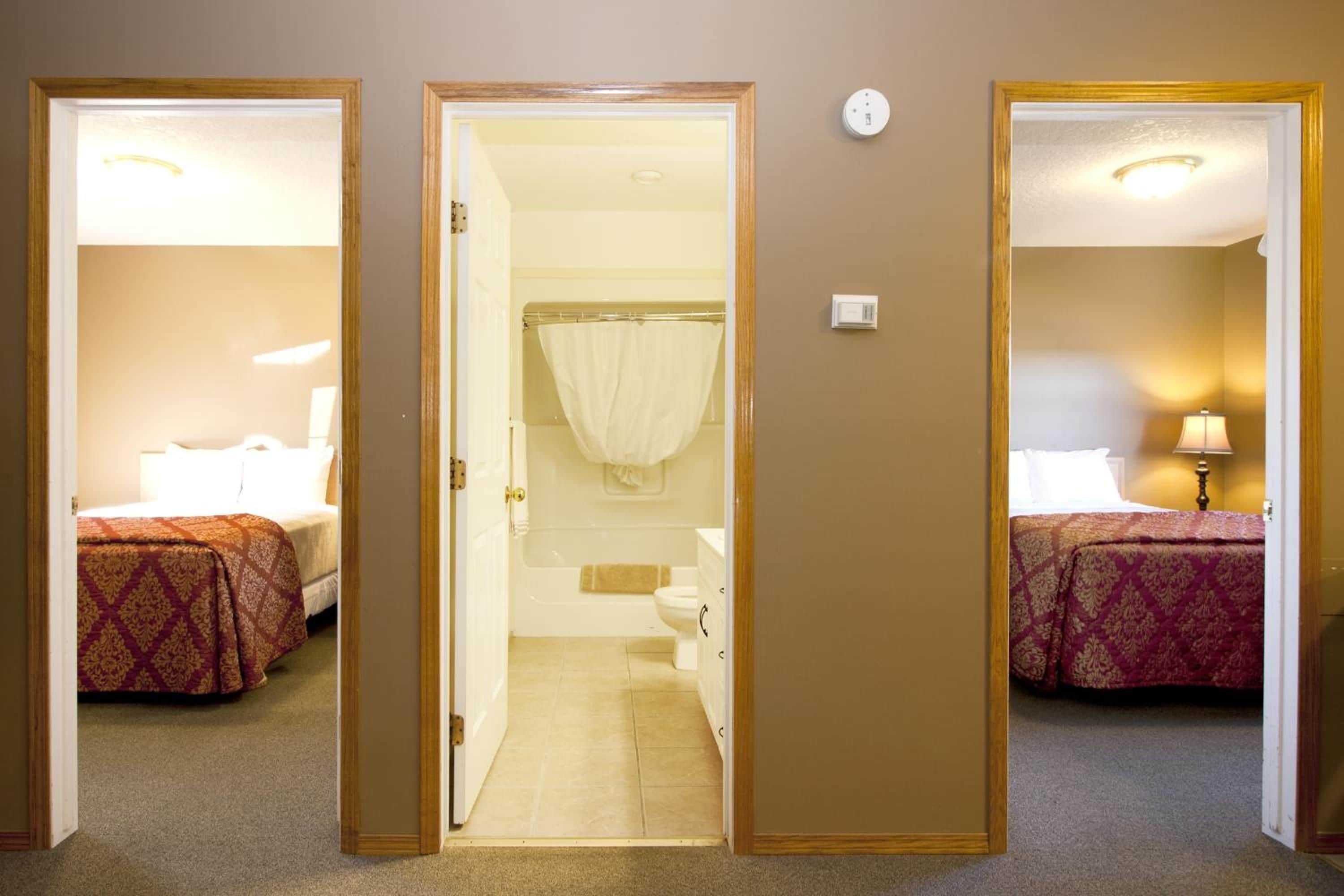 Une chambre d’hôtel avec deux lits, une salle de bain et un couloir.