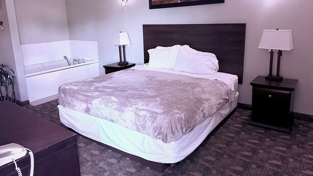 Habitación de hotel con una cama grande, una mesita de noche con lámpara, un baño con lavamanos y un cuadro en la pared.