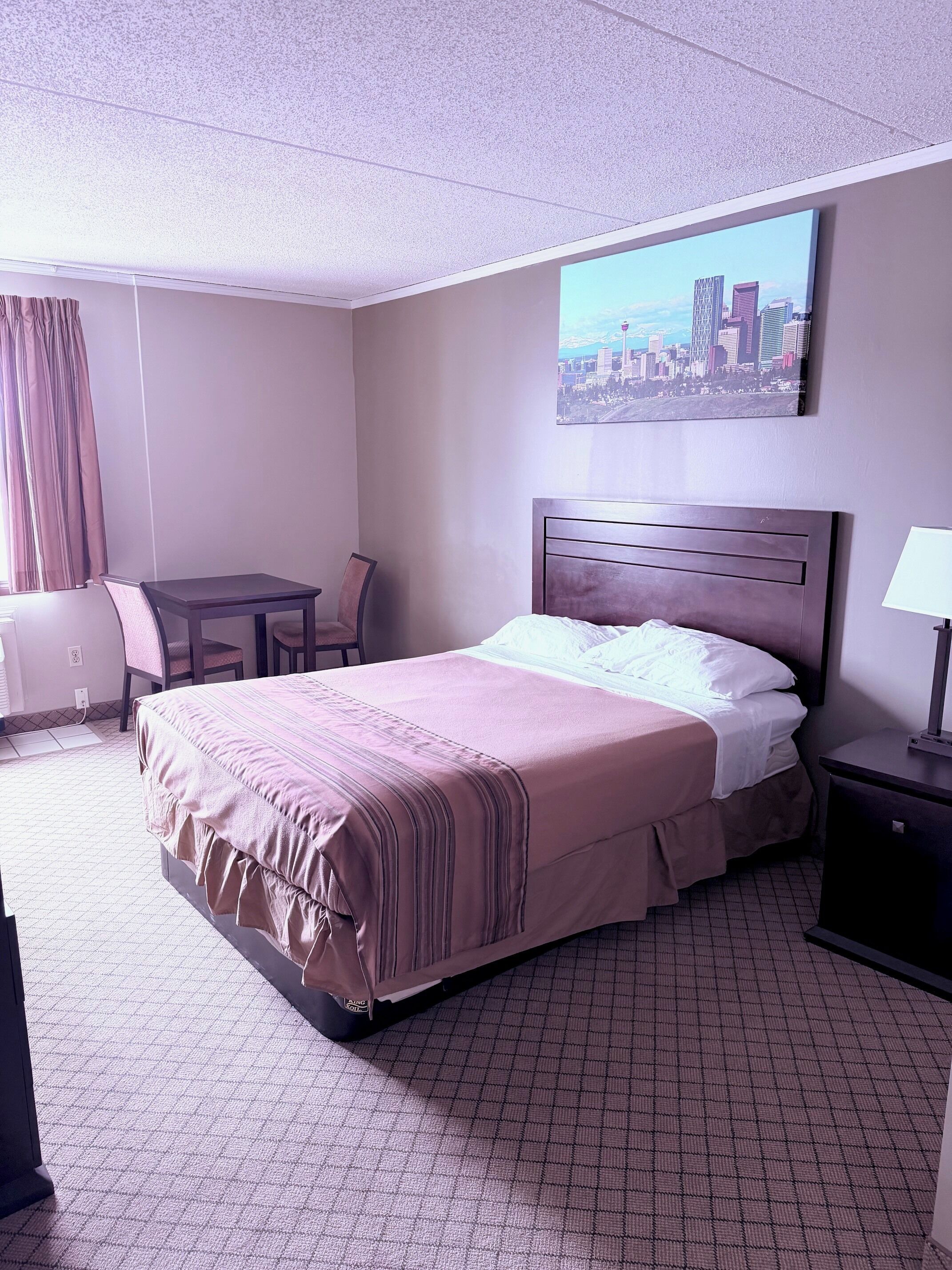 Hotelkamer met een bed, een bureau, een stoel, een nachtkastje en een stadsgezichtschilderij aan de muur.