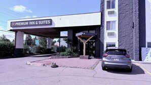 Entrada de un hotel con un letrero que dice 'Premium Inn & Suites', un acceso cubierto y un automóvil estacionado.