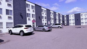 Un estacionamiento con tres coches, un edificio con varias ventanas y un letrero, y un cielo despejado.