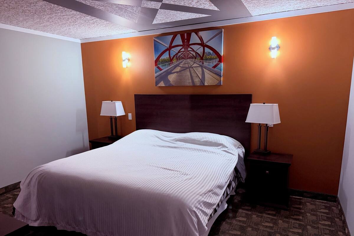 A hotel room with a large bed, two bedside lamps, a painting on the wall, and a patterned carpet.