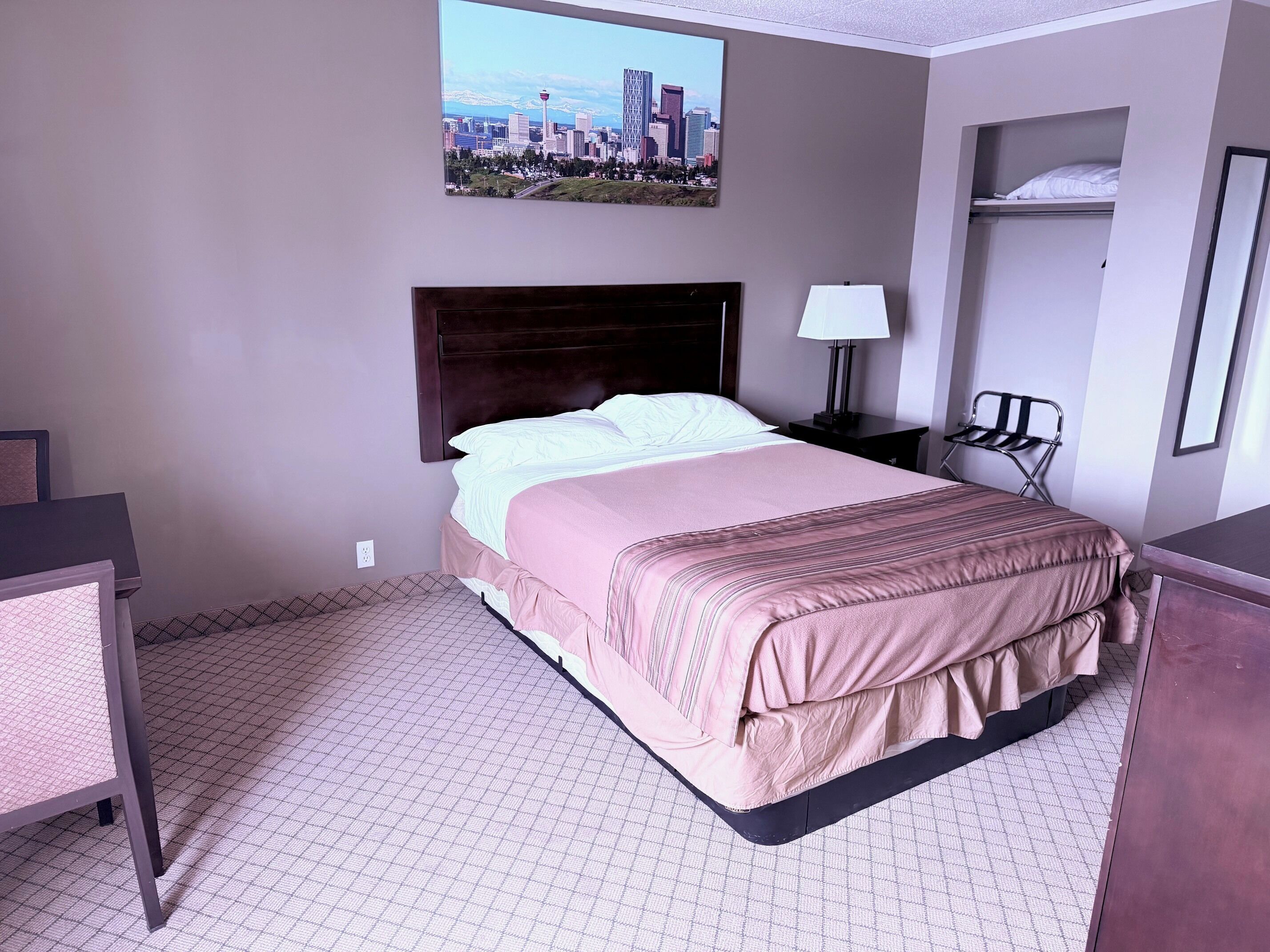 Une chambre d’hôtel avec un lit, un bureau, une chaise, une table de chevet avec une lampe et une vue sur la ville.