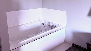 Un baño moderno con una bañera independiente, baldosas blancas y un suelo cubierto de moqueta oscura.