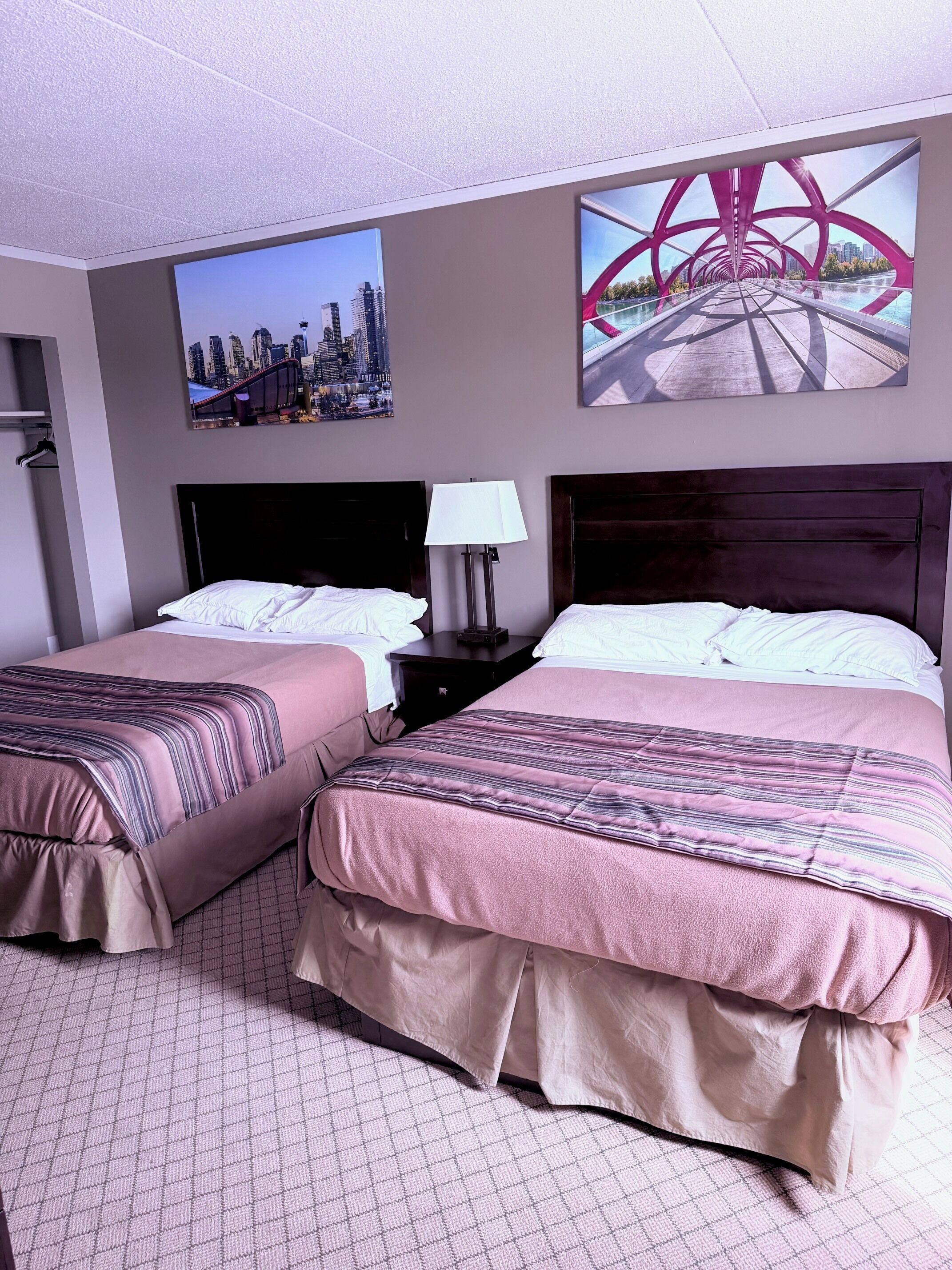 A hotel room with two beds, a nightstand, a lamp, and two wall art pieces.