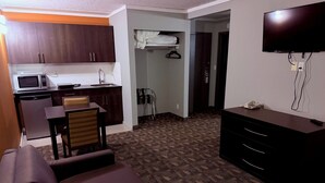 Habitación de hotel compacta con kitchenette, sofá, televisor de pantalla plana y vestidor.