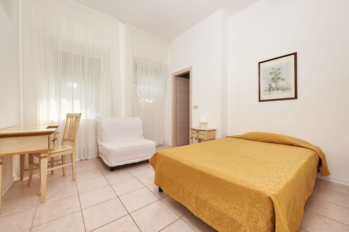 Een hotelkamer met een bed, stoel, bureau en een deur.