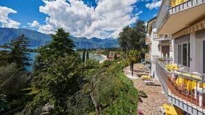 Un balcon d’hôtel avec des tables et des chaises jaunes, donnant sur un lac et des montagnes.