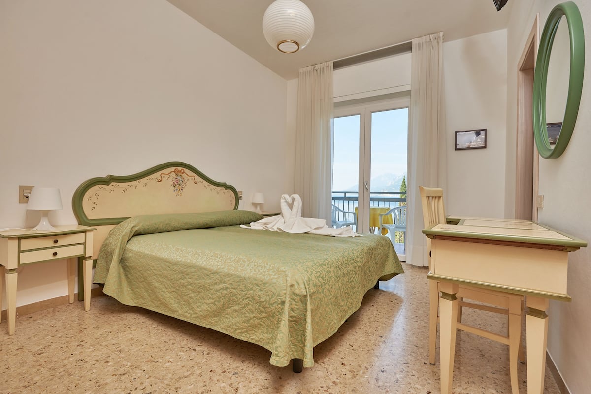 Een hotelkamer met een bed, een bureau, een stoel, een raam met gordijnen en uitzicht op zee.