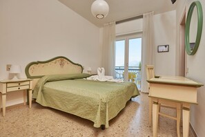 Habitación de hotel con cama, escritorio, silla, ventana con cortinas y vista al mar.