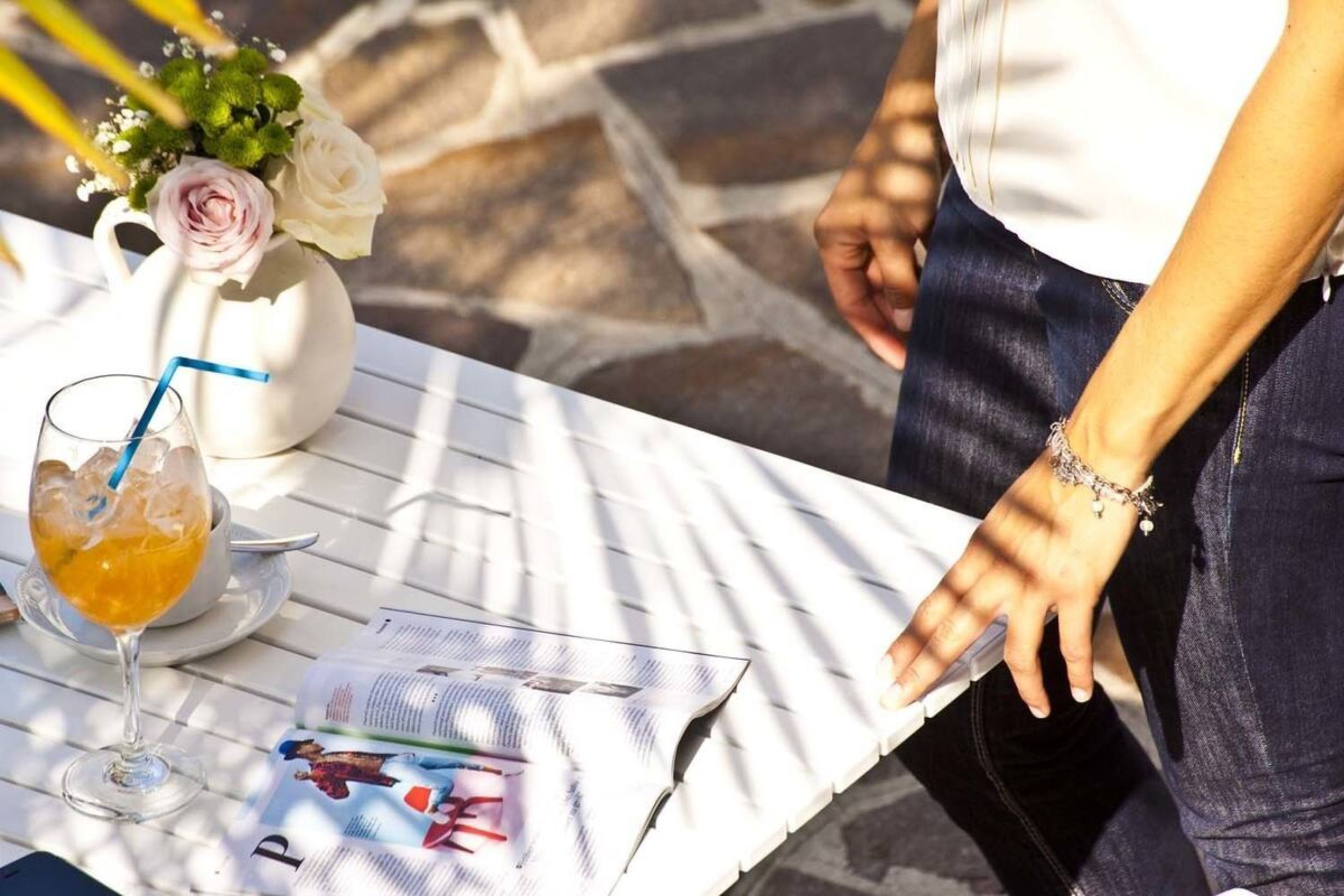 A table with a drink, a pitcher of flowers, and a magazine.