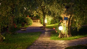 Un chemin de pierres qui traverse un jardin agrémenté de plantes en pot et d’un panneau indicateur.