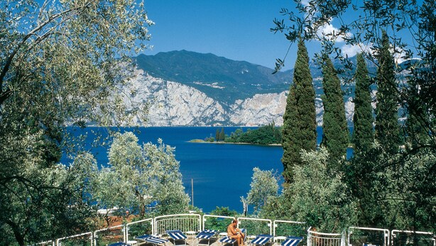 Un espace piscine doté de chaises longues et offrant une vue sur un lac et des montagnes.