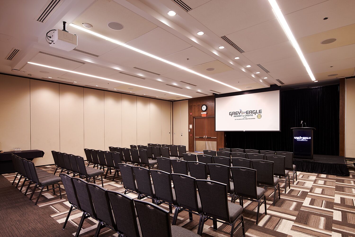 A conference room with rows of chairs, a stage with a podium, and a screen displaying 'GREY EAGLE RESORT & CASINO'.