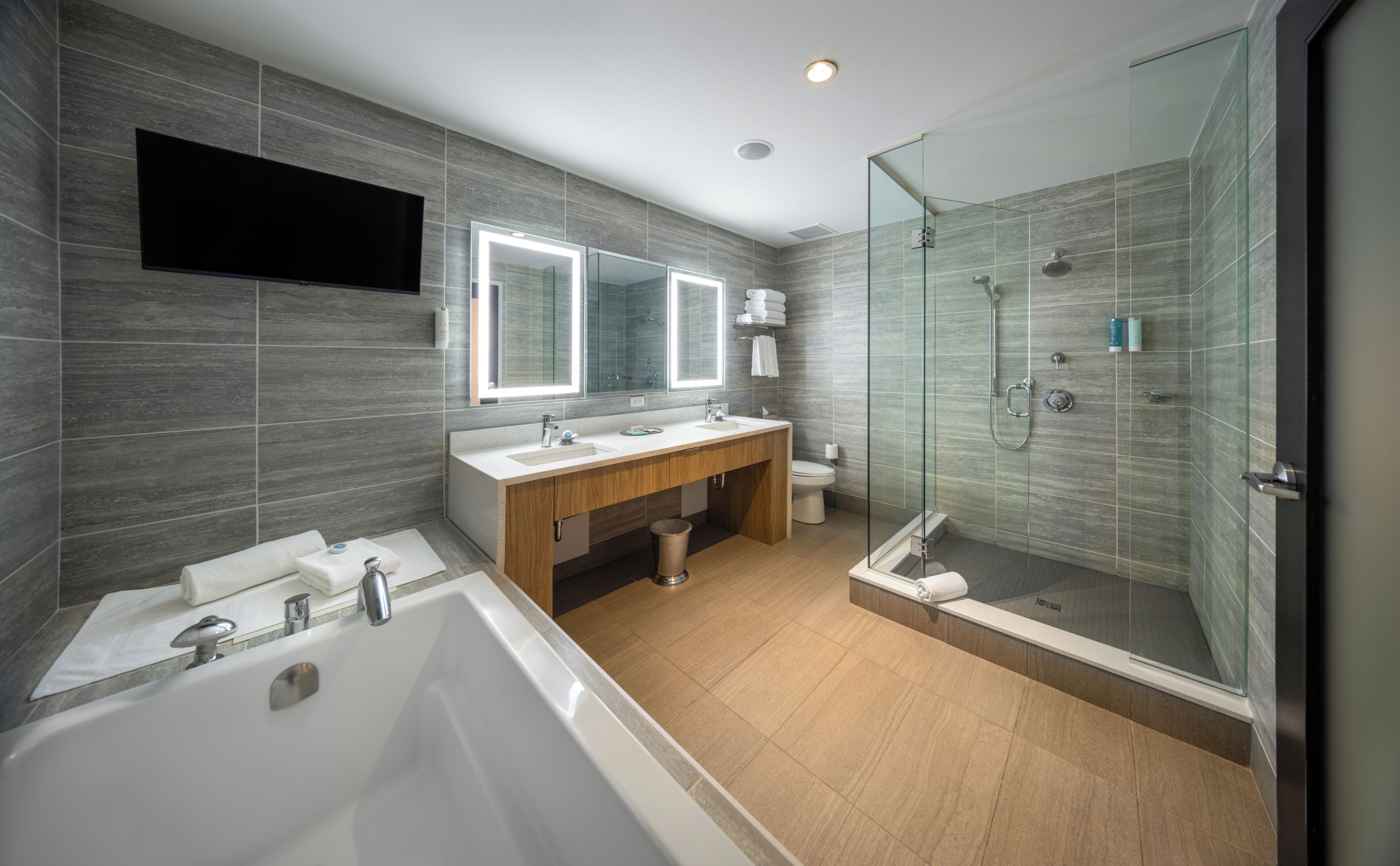 A modern bathroom with a bathtub, two sinks, a vanity, a glass shower enclosure, and a large mirror.