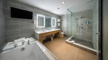 A modern bathroom with a bathtub, two sinks, a vanity, a glass shower enclosure, and a large mirror.