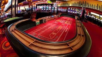 A craps table in a casino with multiple slot machines and a vibrant, circular carpet design.