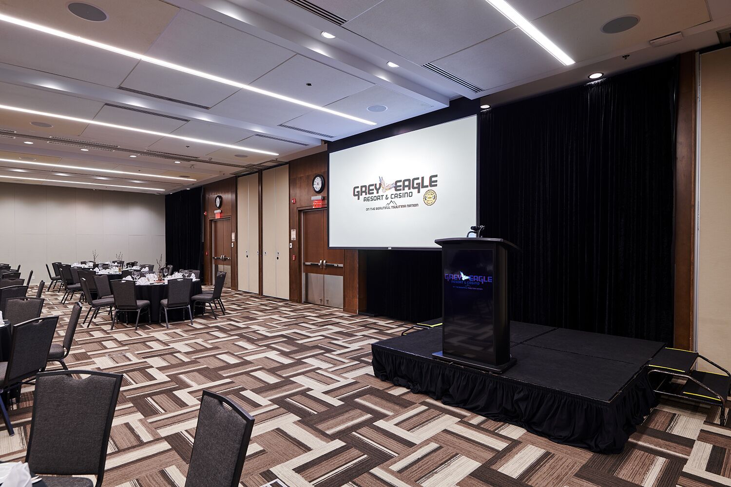 A conference room with a presentation screen, a podium, and rows of chairs.