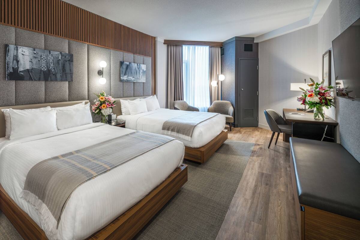 Habitación de hotel con dos camas, un escritorio, una silla y un televisor.