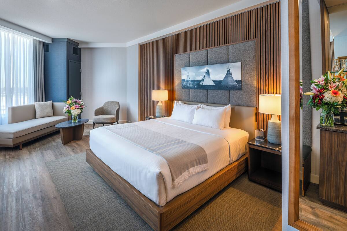 Habitación de hotel con cama, sofá, sillón, una mesita y escritorio con lámpara.