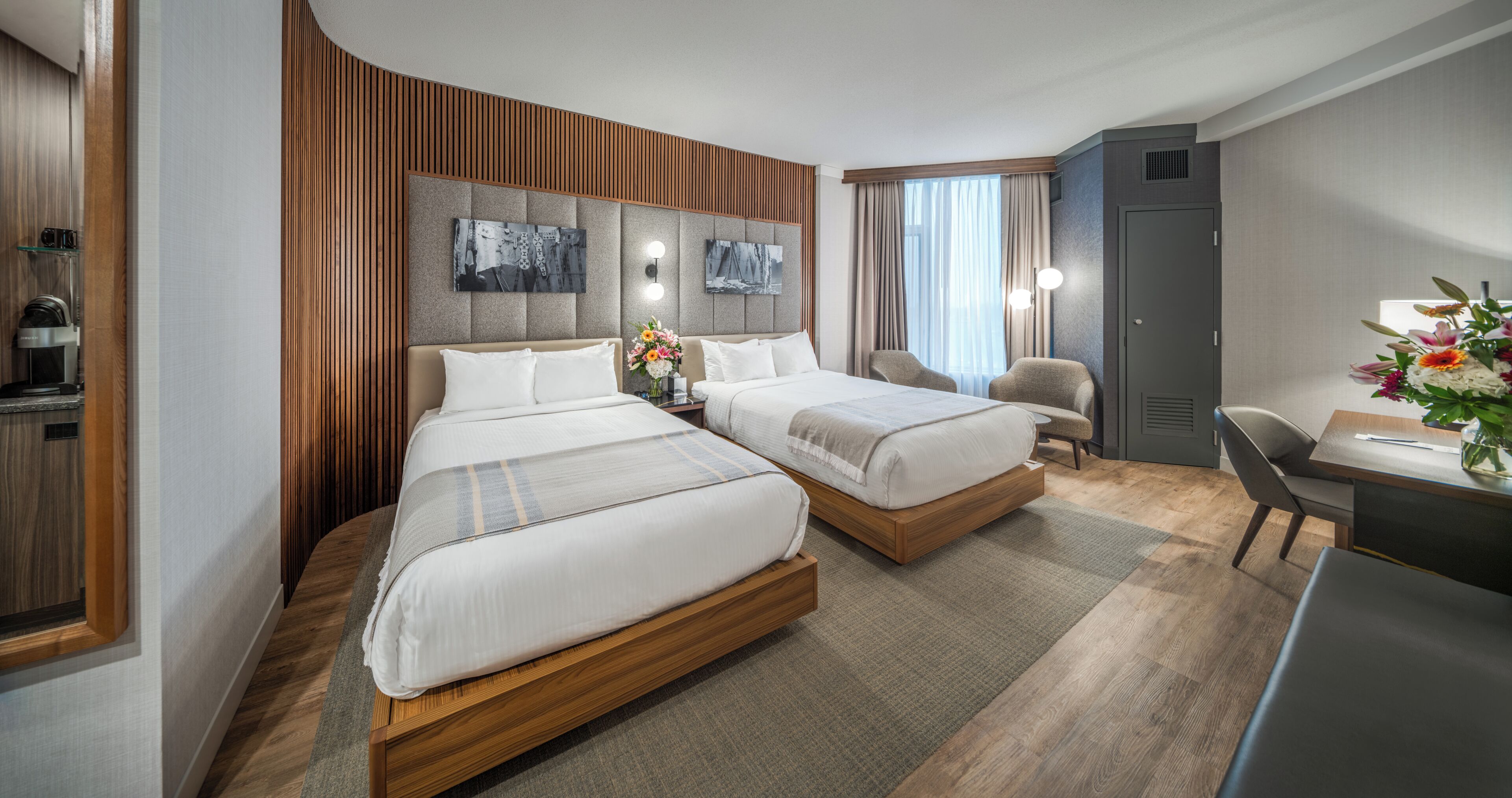 Habitación de hotel con dos camas, un escritorio, una silla, una cafetera y obras de arte en la pared.