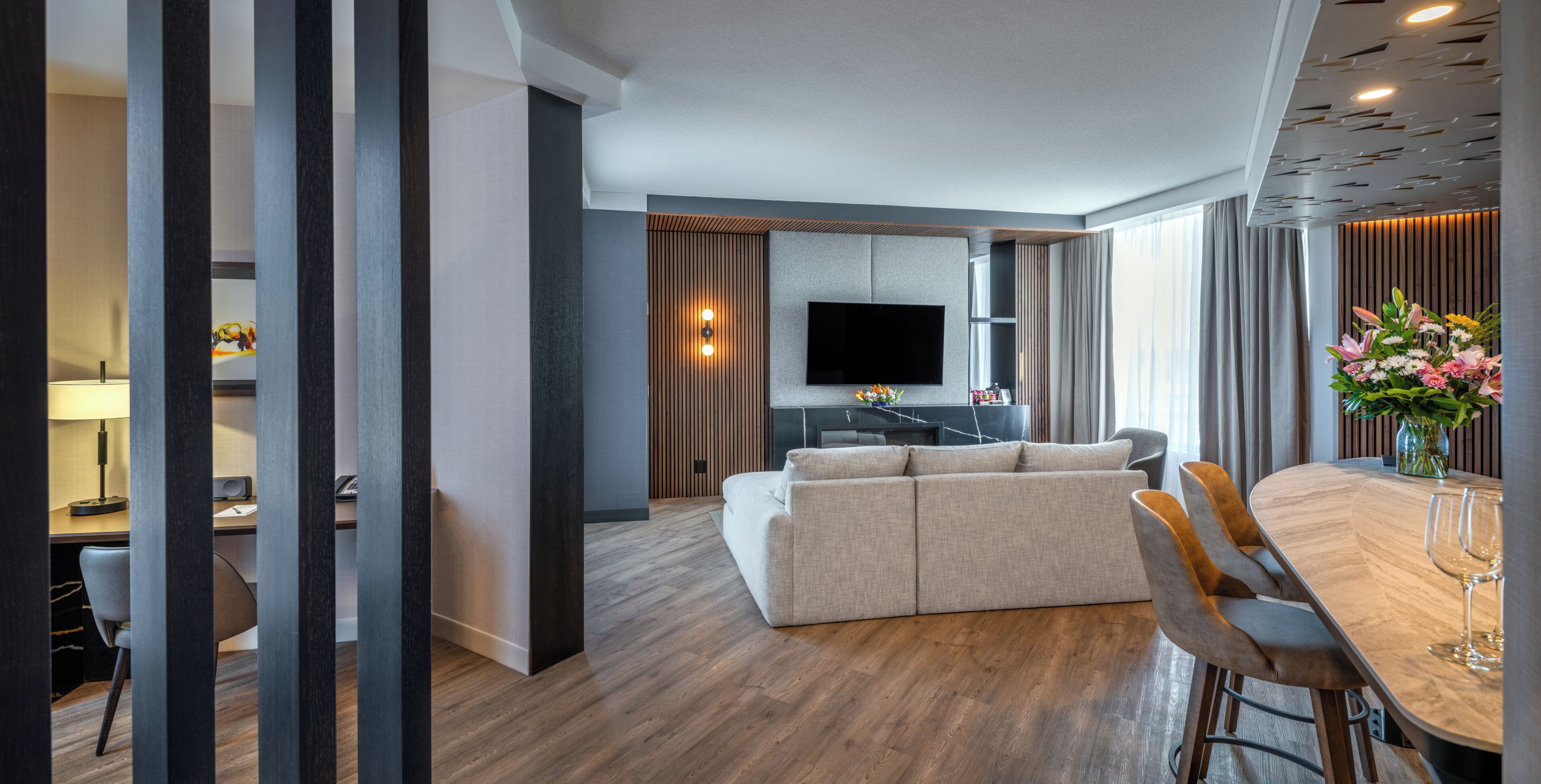 Una sala de estar moderna con un sofá, una mesa de comedor con sillas, un televisor de pantalla plana y un jarrón decorativo con flores.