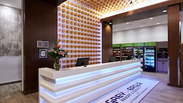 Un mostrador de recepción de diseño moderno, una pared con un patrón geométrico y máquinas expendedoras que ofrecen tentempiés y bebidas.