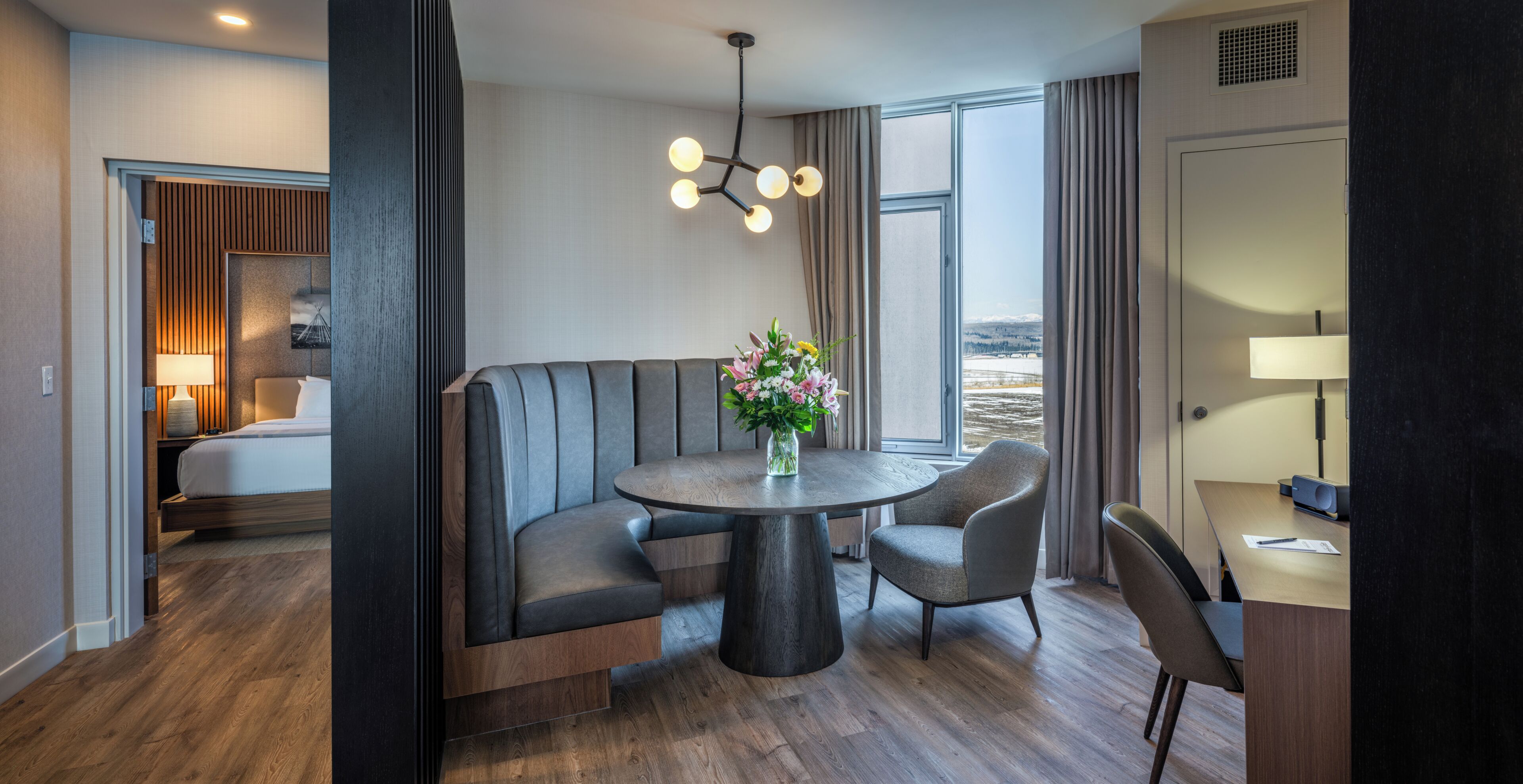 Ein Hotelzimmer mit Bett, einer Sitzecke mit Tisch, einem Schreibtisch und Blick auf eine verschneite Landschaft.