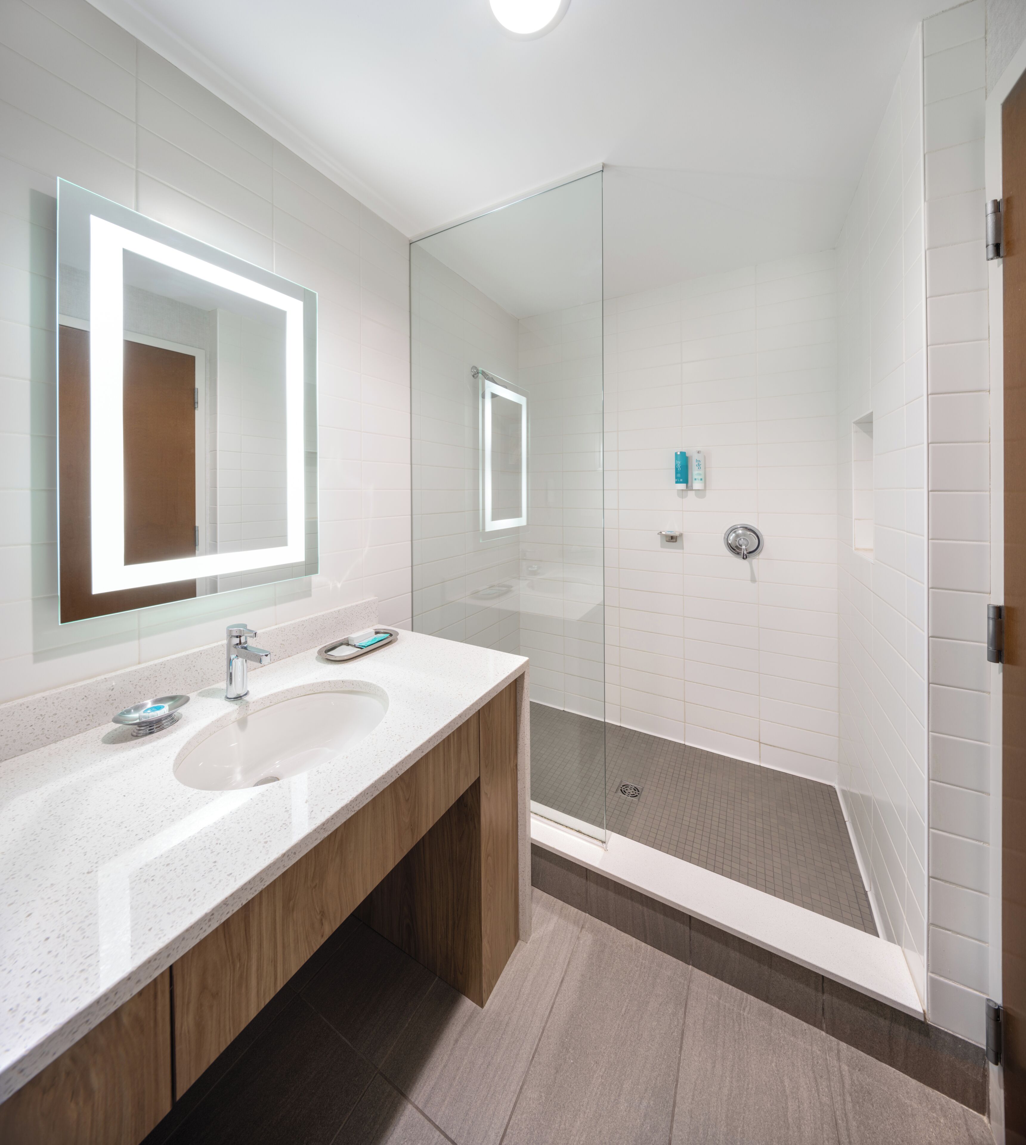 A modern bathroom with a glass-enclosed shower, a large mirror, and a wooden vanity.
