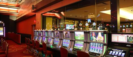 Un salón de casino con numerosas máquinas tragamonedas y sillas rojas.