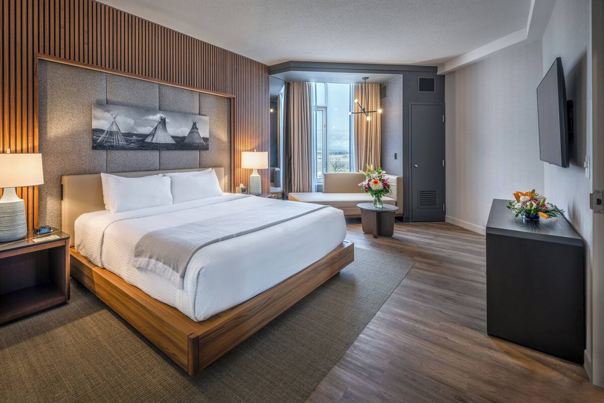 Habitación de hotel con una cama grande, un escritorio, una silla, un televisor y una ventana con cortinas.