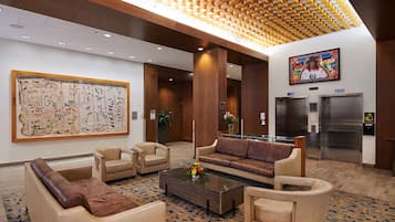 A lobby with a large indigenous artwork, seating area, elevators, and a modern ceiling design.