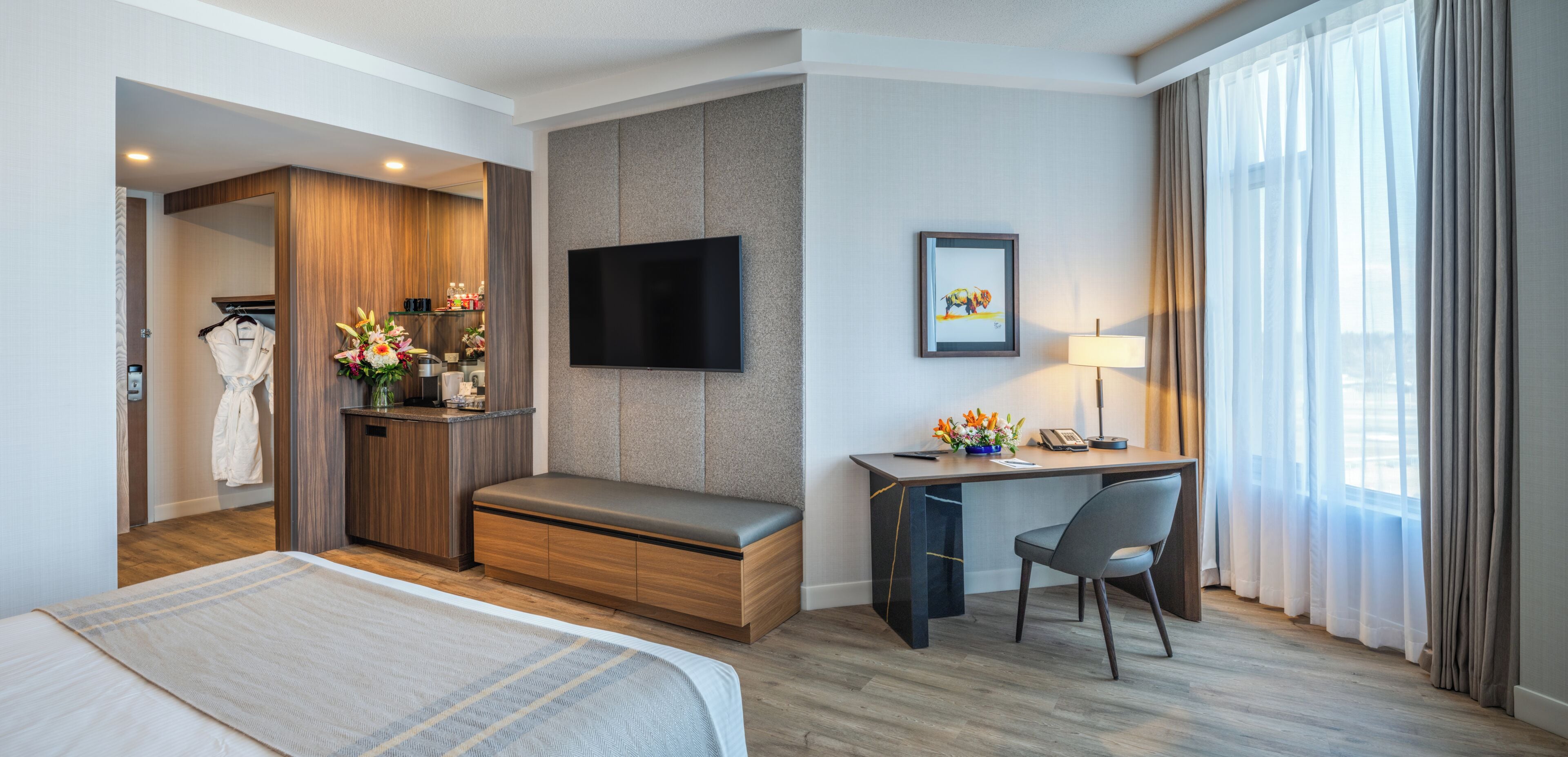 A hotel room with a bed, a desk with a chair, a TV, a framed picture, and a window with curtains.