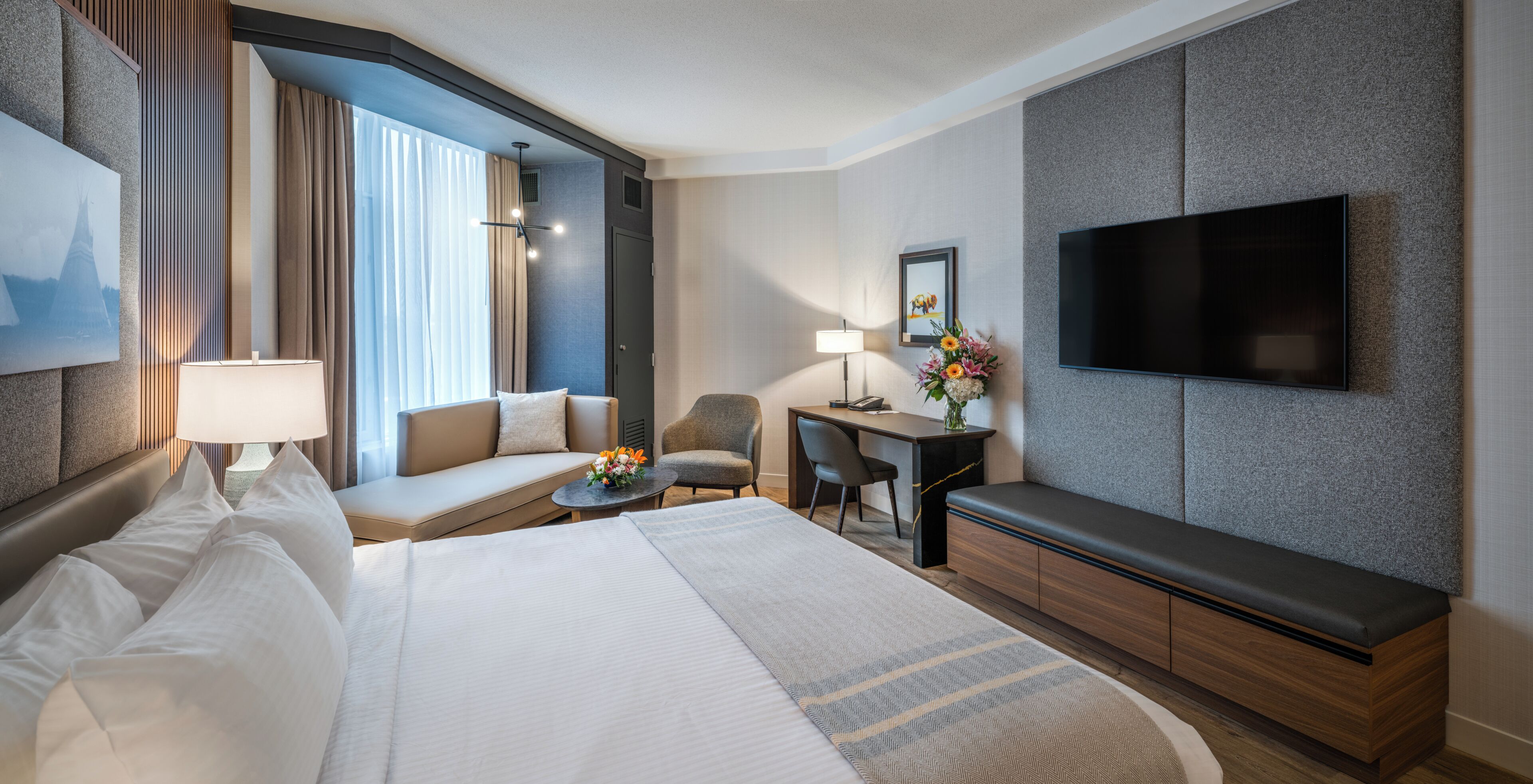 Habitació d'hotel amb llit, escriptori, cadira, sofà, televisió i finestra amb cortines.