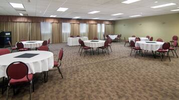 Un salón de conferencias con varias mesas redondas y sillas, piso alfombrado y cortinas en las ventanas.