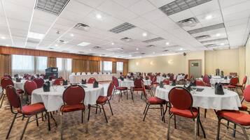 A conference room with multiple round tables, red chairs, and white tablecloths.