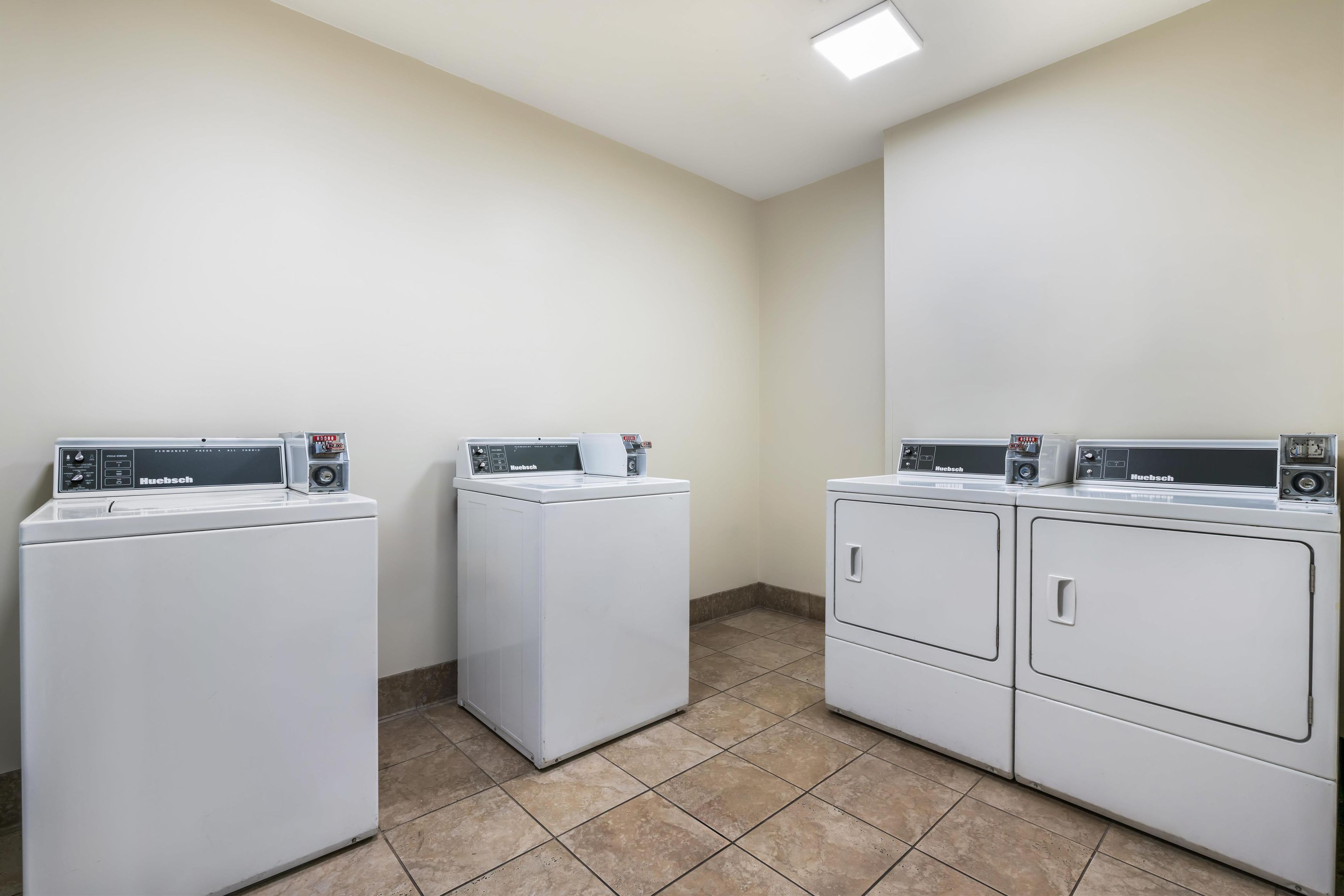 A laundry room with three white front-loading washing machines and dryers.