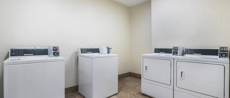 A laundry room with three white front-loading washing machines and dryers.